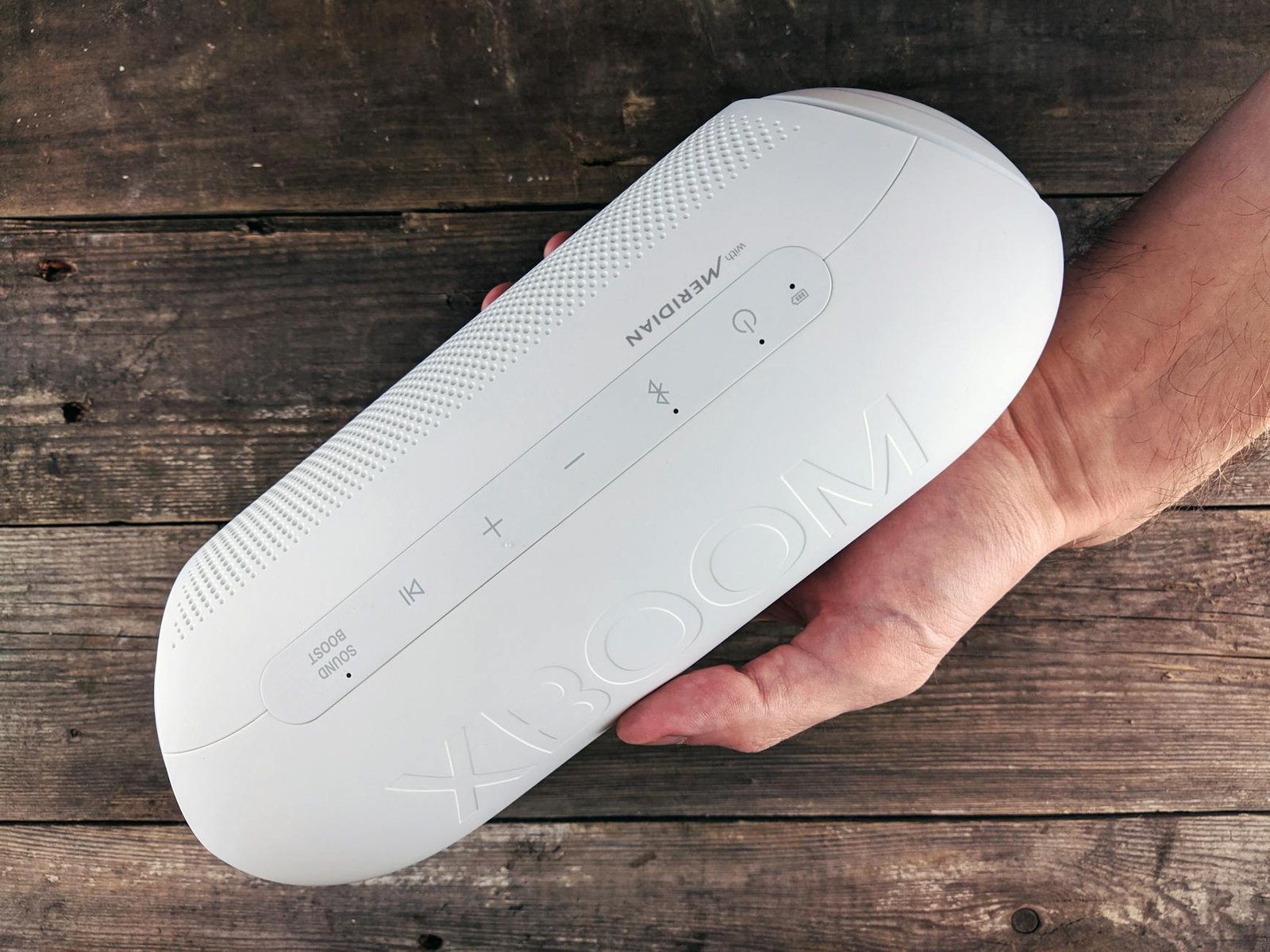White Bluetooth speaker held by a hand on a wooden surface, showcasing detail and texture.