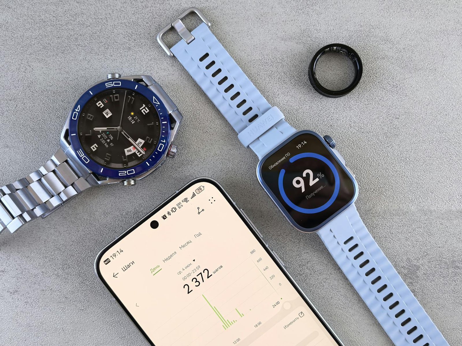 Smartwatch, ring tracker, and smartphone displaying fitness data on a gray surface.