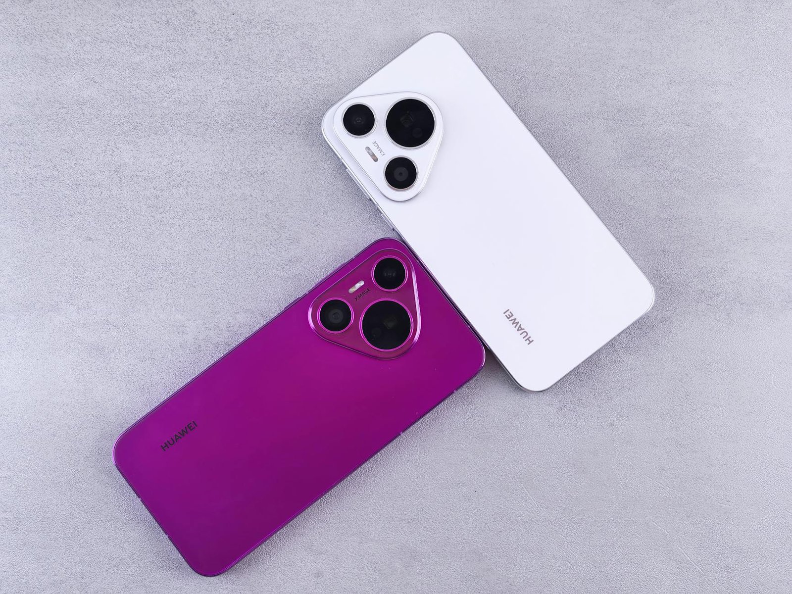 Two Huawei smartphones, one white and one purple, on a textured concrete surface.