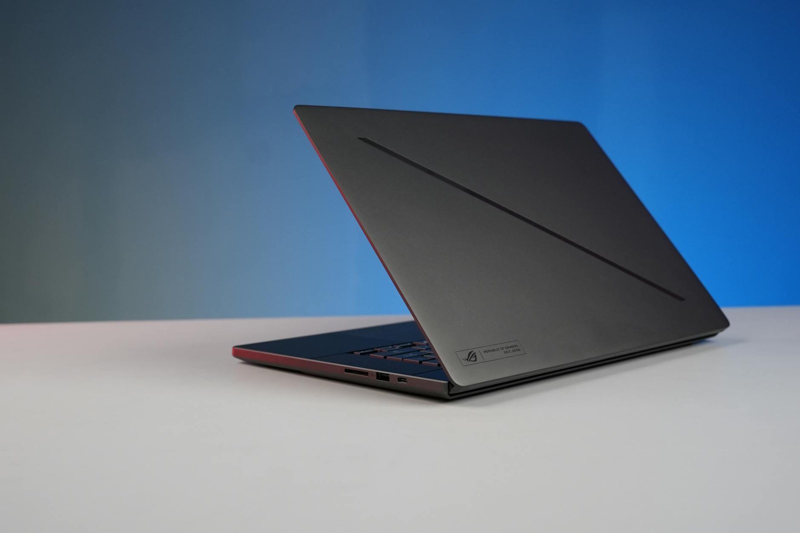 Elegant black laptop on a minimalist desk with a gradient blue background, perfect for tech and work concepts.