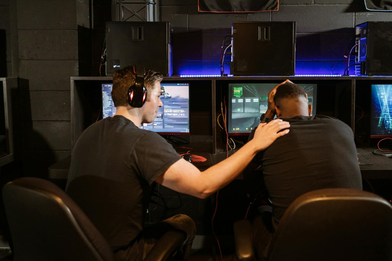 Two gamers support each other in a cyber cafe, navigating challenges together.