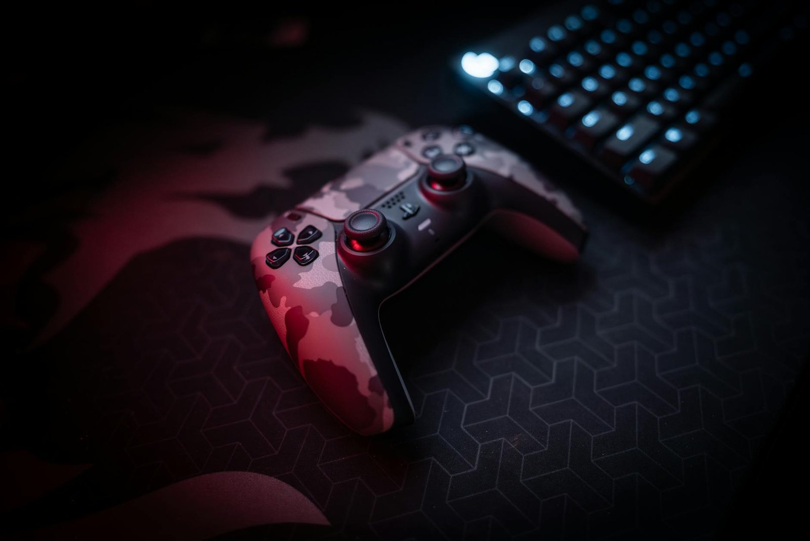 Close-up of a camouflage gaming controller and keyboard with red lighting ambiance.