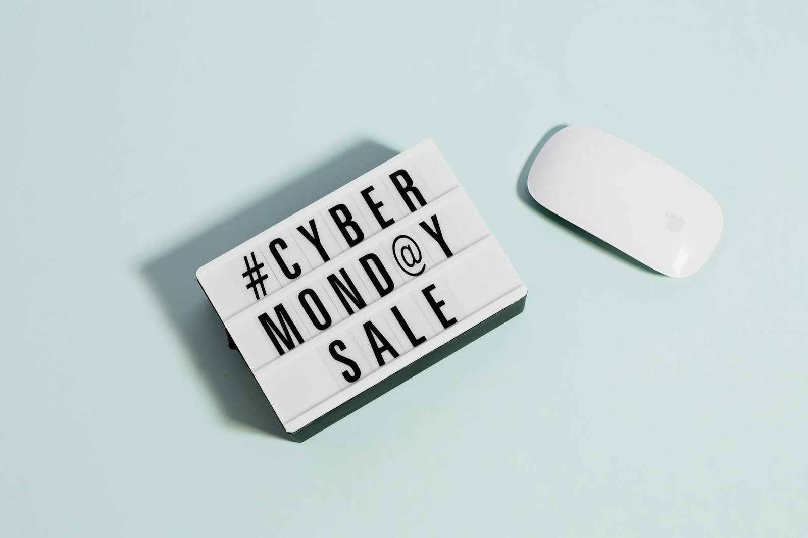 Lightbox sign displaying 'Cyber Monday Sale' beside a computer mouse on a pastel background.