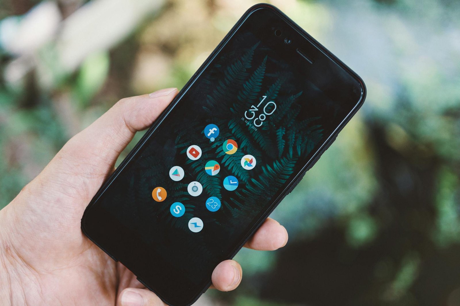 Close-up of a hand holding a smartphone with app icons and a nature wallpaper.