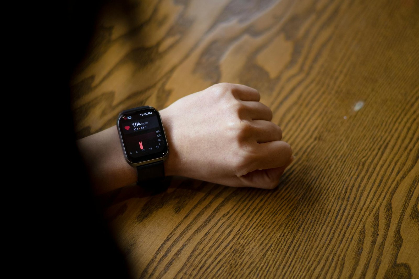 A person checks heart rate on smartwatch showing 104 bpm on wooden table.