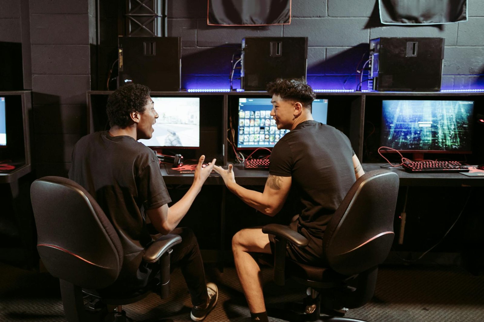 Two friends chatting while playing games in a modern internet cafe.
