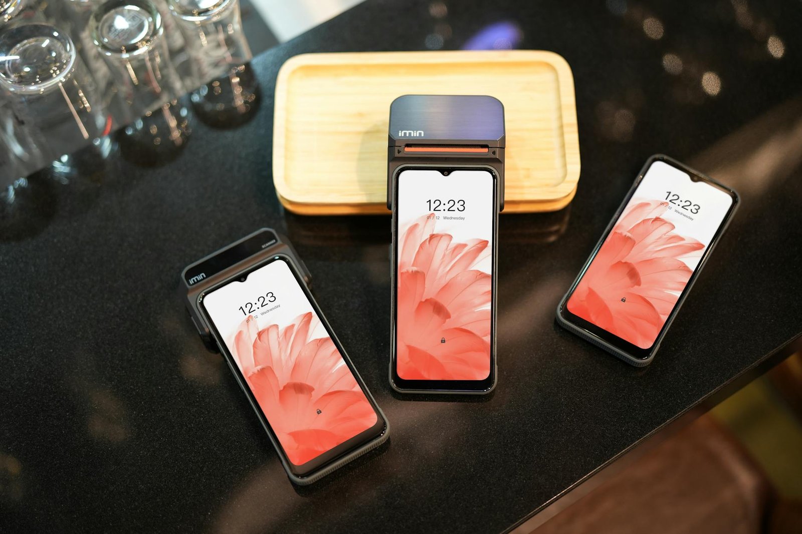 Close-up of three modern smartphones displaying a floral wallpaper, placed on a black surface.