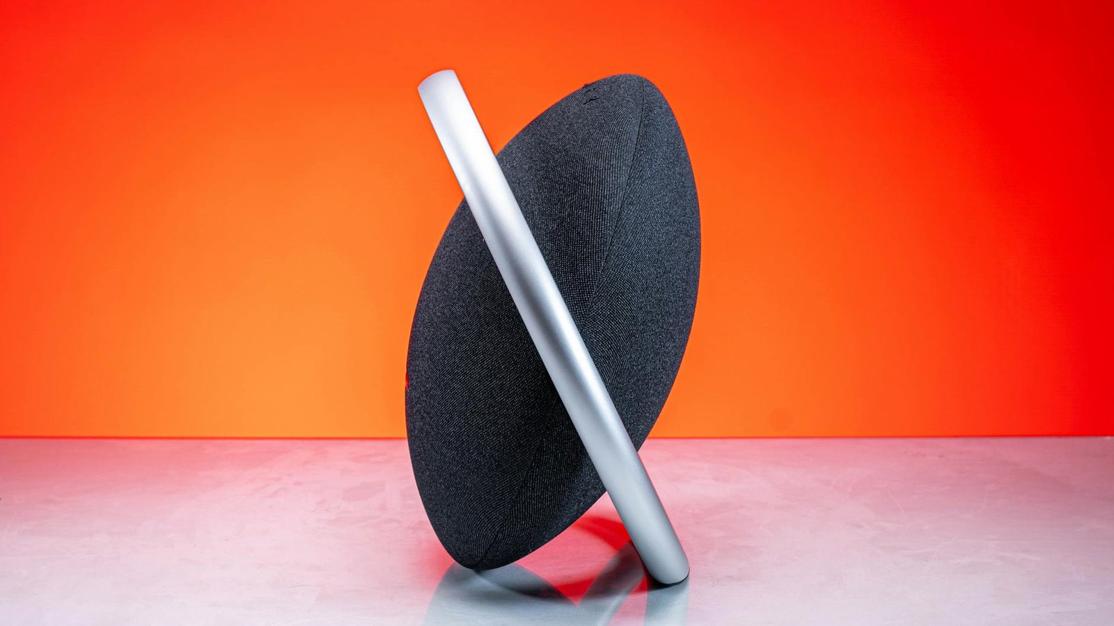 Contemporary wireless speaker set against a vivid orange backdrop, showcasing sleek design.