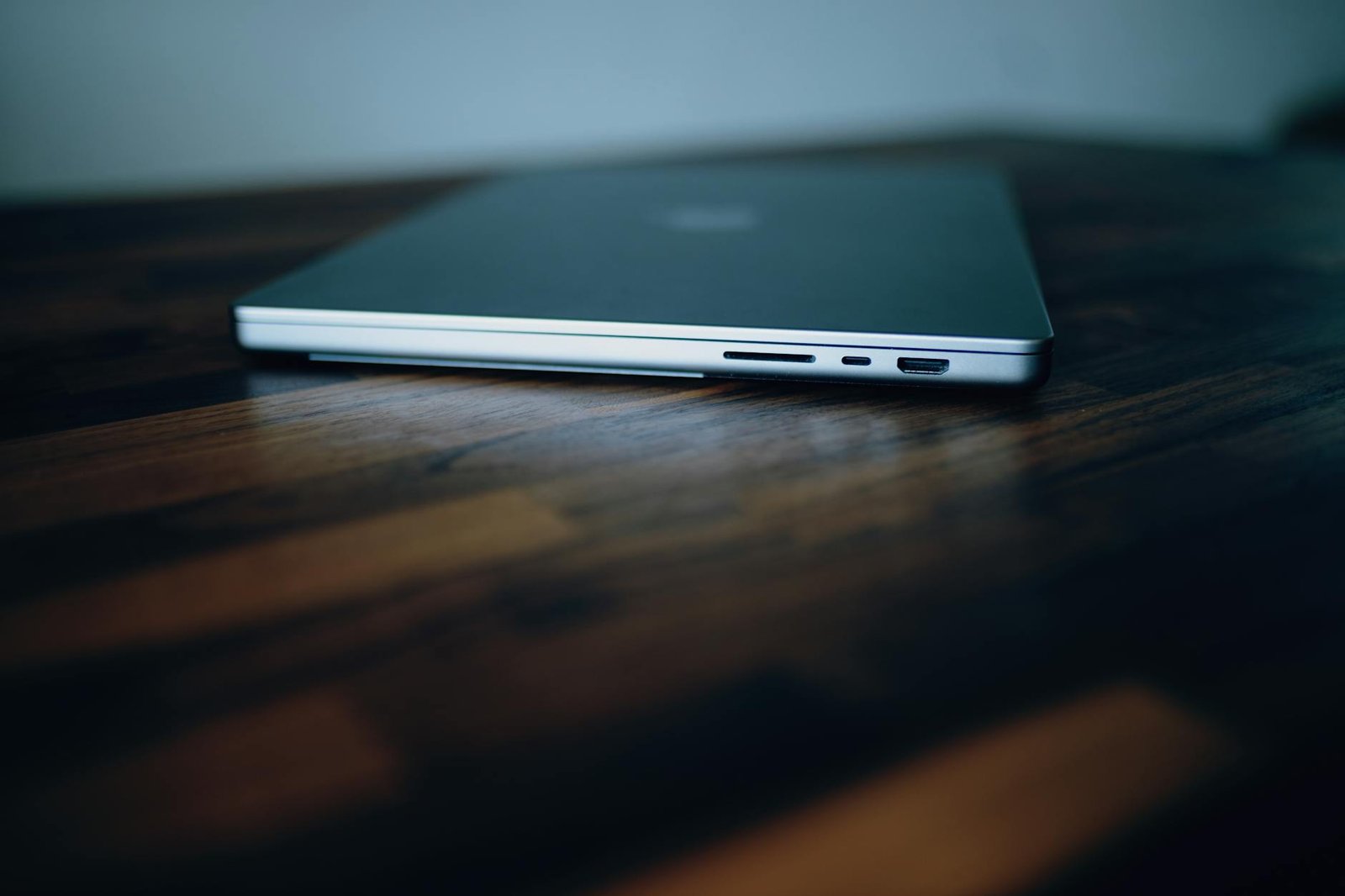 Side view of a closed laptop showing its ports on a stylish wooden surface.