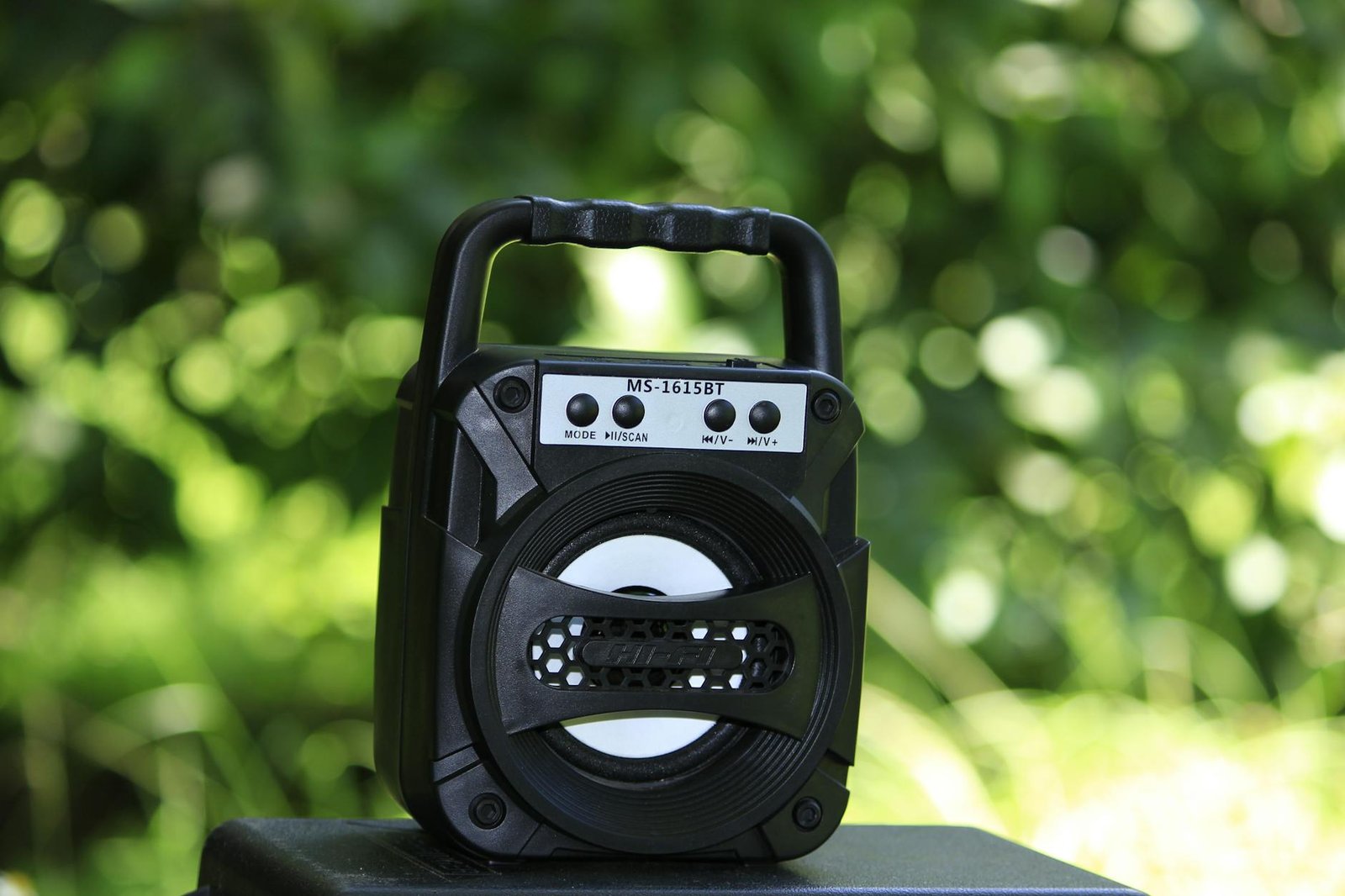 Close-up of a portable wireless speaker against a blurred green outdoor background.