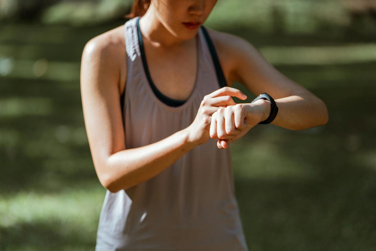 A woman in activewear checks her smart fitness tracker outdoors on a sunny day.