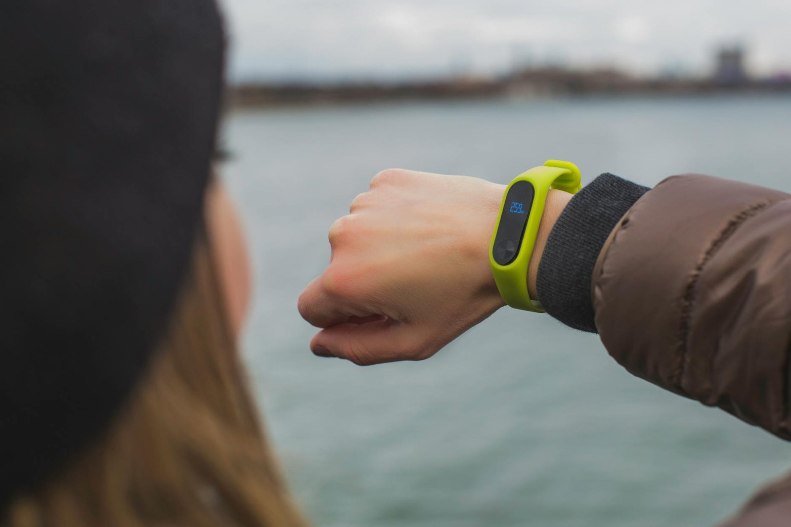 Close-up of a woman outdoors checking the time on her smartwatch by a lake.