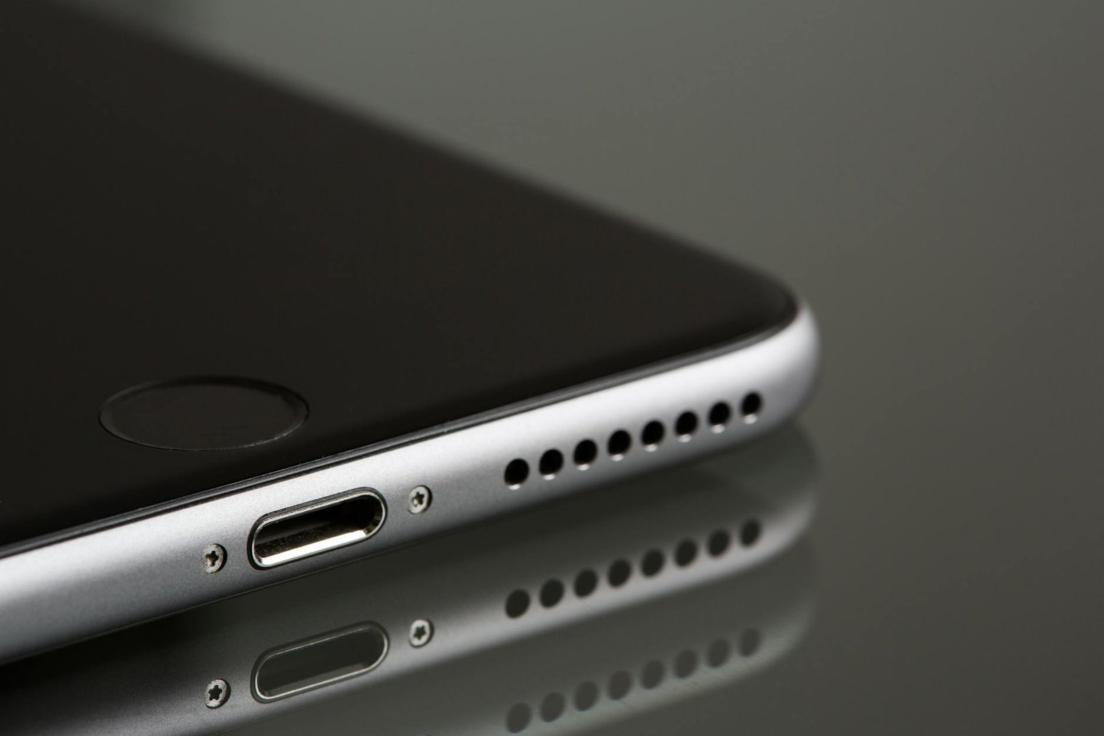 A sleek smartphone close-up highlighting its lightning connector and speaker, reflecting on a surface.
