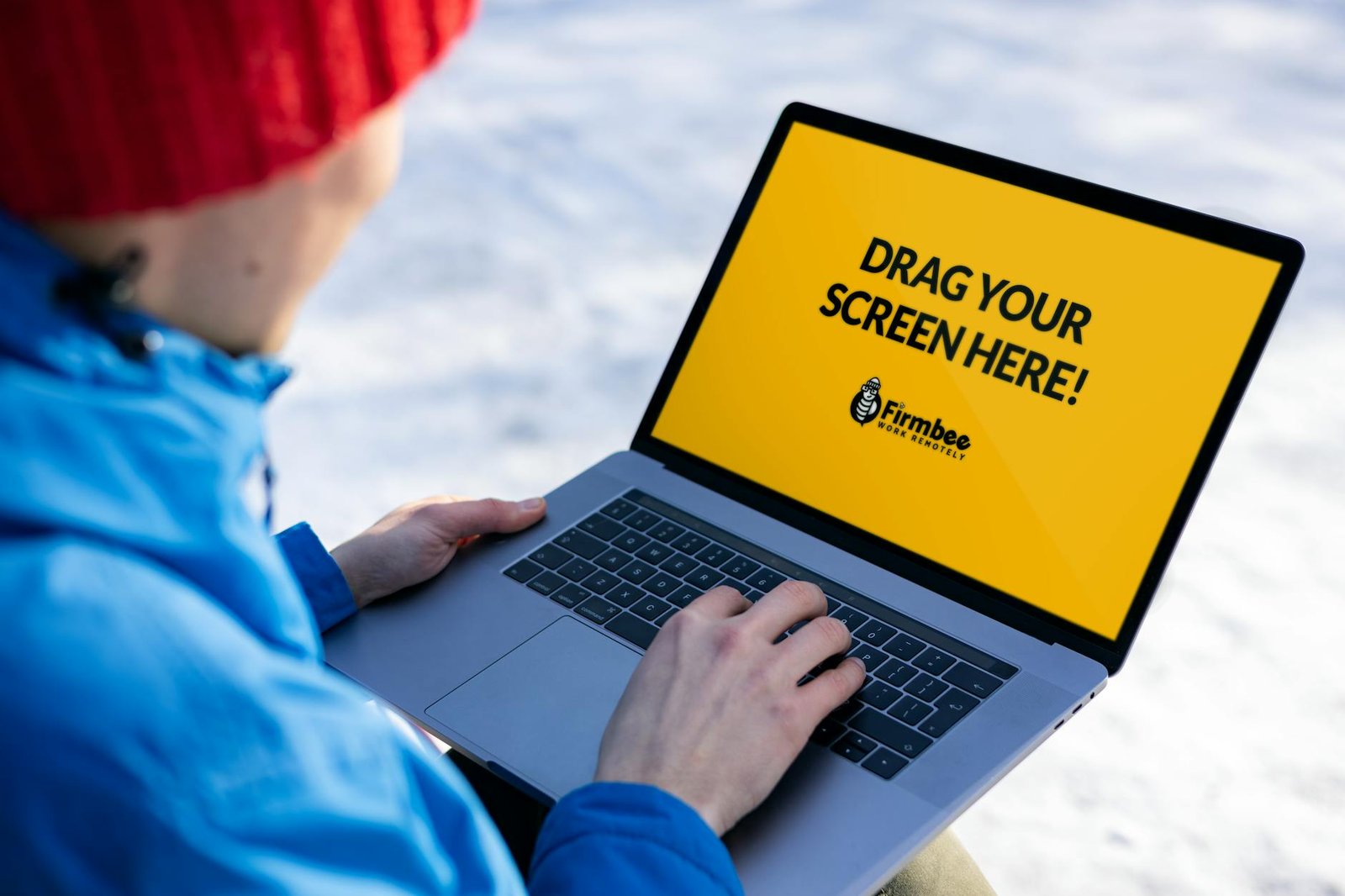 Individual in red hat using a laptop with mockup screen outdoors on a snowy day.