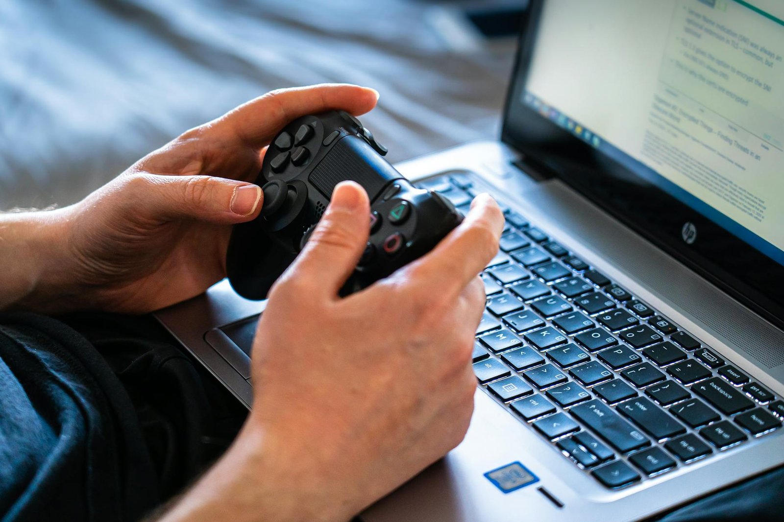 Person holds a gaming controller while interacting with a laptop, emphasizing modern gaming technology.
