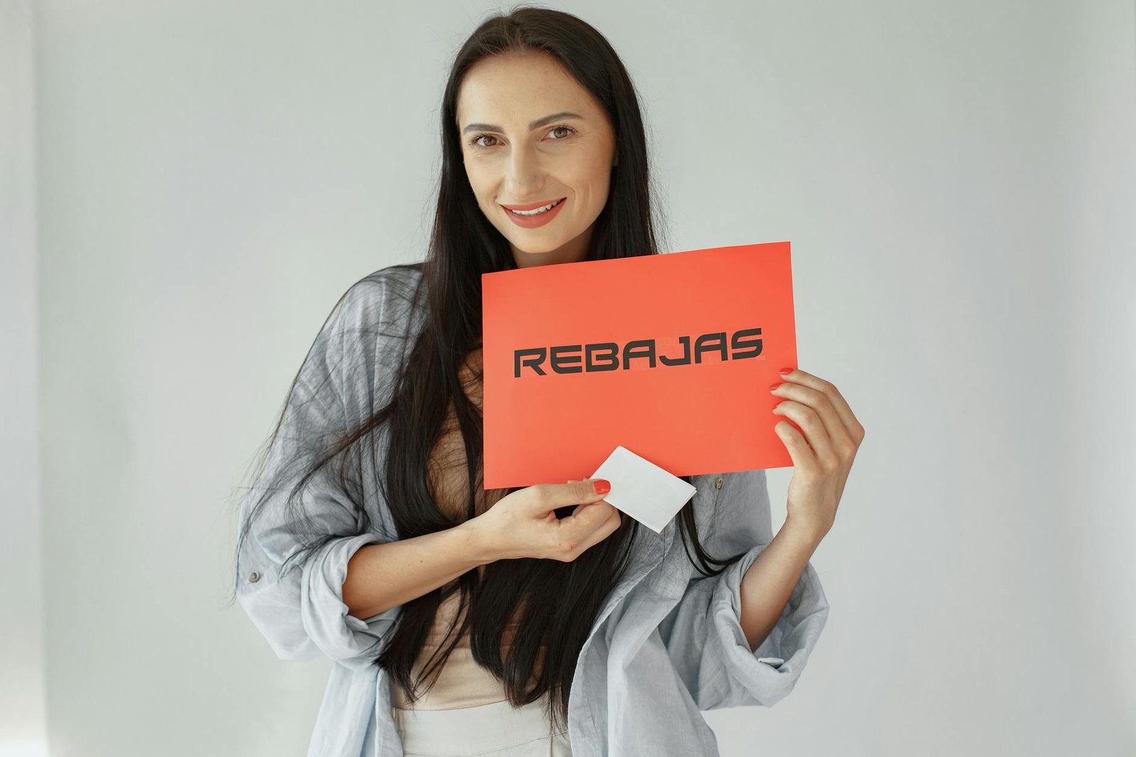Smiling woman holds a red 'REBajas' sign, promoting sales and discounts.