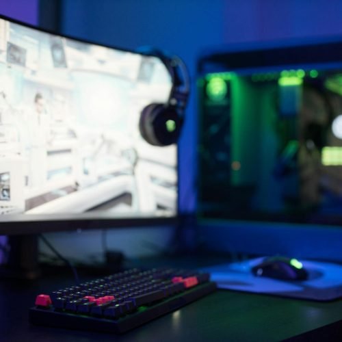 High-tech gaming setup featuring a curved monitor, RGB keyboard, and vibrant lighting.