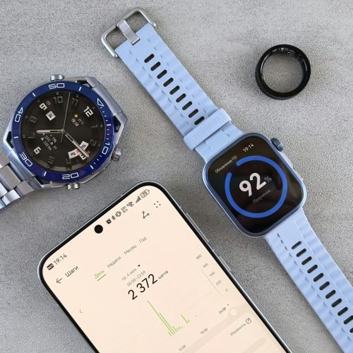 Smartwatch, ring tracker, and smartphone displaying fitness data on a gray surface.