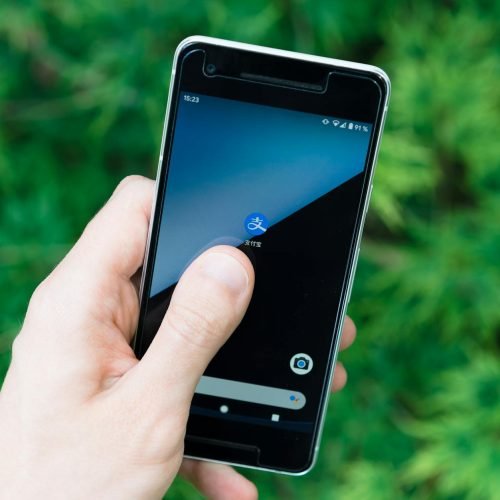 Hand holding smartphone with app icon on screen, showcasing modern technology outdoors.