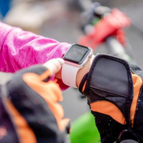 Close-up of a cyclist wearing gloves checking a smartwatch outdoors.