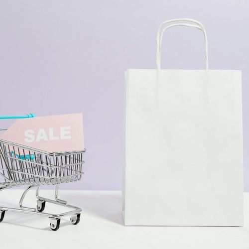 A miniature shopping cart with a sale sign beside a paper bag, perfect for online shopping themes.