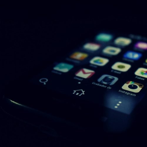 Dark-themed close-up of a smartphone screen highlighting various apps and touchscreen technology.