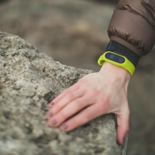 Close-up of a hand with a fitness tracker touching a rock outdoors, showcasing exploration.