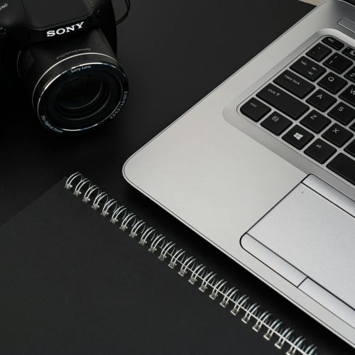 A stylish office desk featuring a laptop, camera, and spiral notebook on a dark surface.