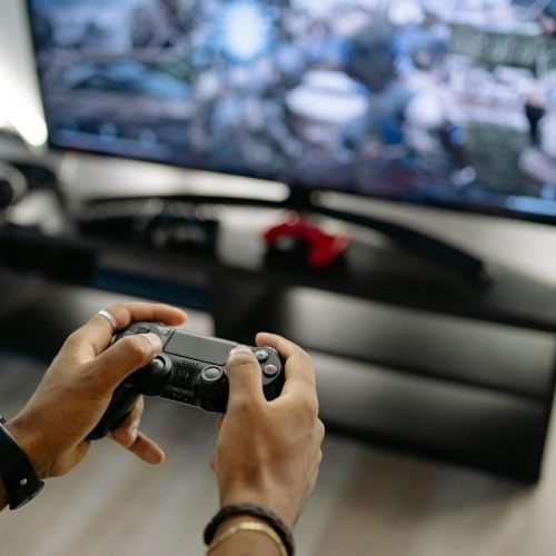Close-up of hands holding a gaming controller while playing video games indoors.