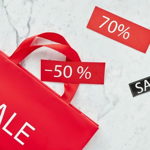 Red sale bag with 50% and 70% discount tags on marble background, perfect for retail promotions.