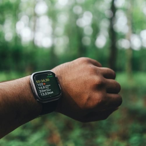 Close-up of a hand wearing a smartwatch with blurred forest background, showing fitness metrics.