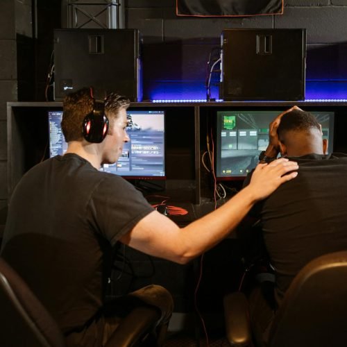 Two gamers support each other in a cyber cafe, navigating challenges together.