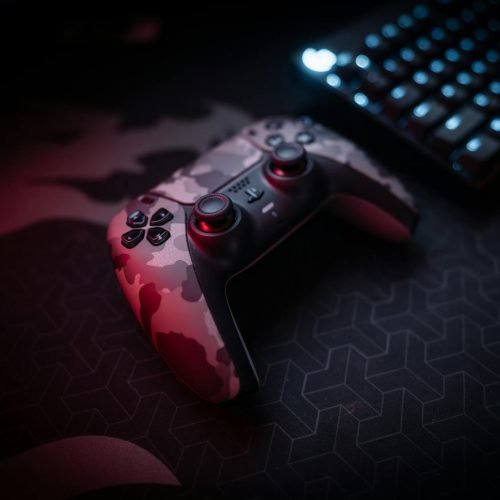 Close-up of a camouflage gaming controller and keyboard with red lighting ambiance.