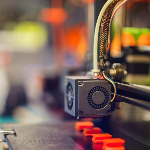 Detailed close-up of a 3D printer extruding red plastic during operation.