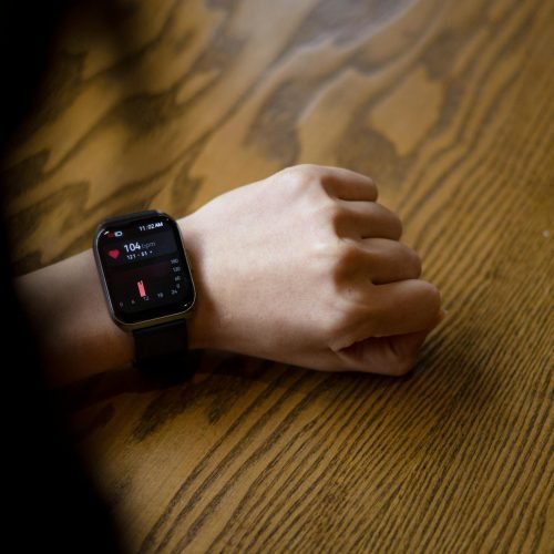 A person checks heart rate on smartwatch showing 104 bpm on wooden table.