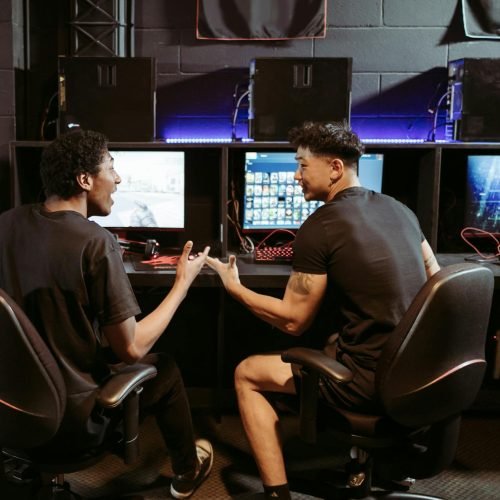 Two friends chatting while playing games in a modern internet cafe.