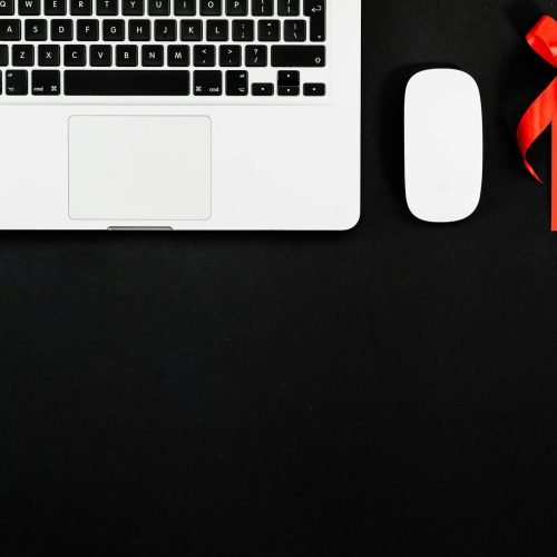 Top view of laptop, wireless mouse, and red sale tag on black surface.