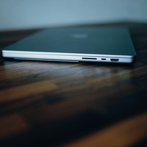 Side view of a closed laptop showing its ports on a stylish wooden surface.