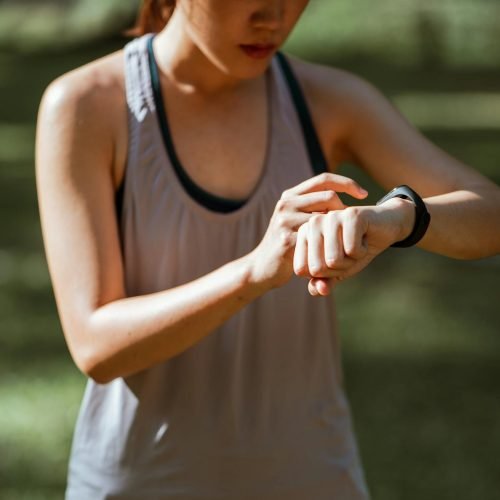 A woman in activewear checks her smart fitness tracker outdoors on a sunny day.