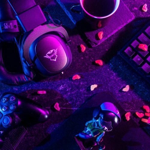 Colorful flat lay of gaming gear including headset, controller, and keyboard under vibrant lighting.