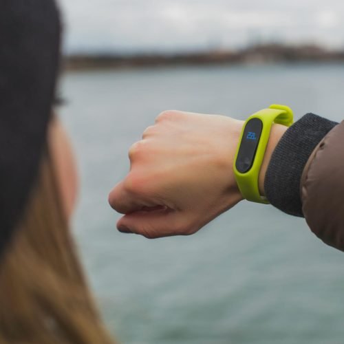 Close-up of a woman outdoors checking the time on her smartwatch by a lake.