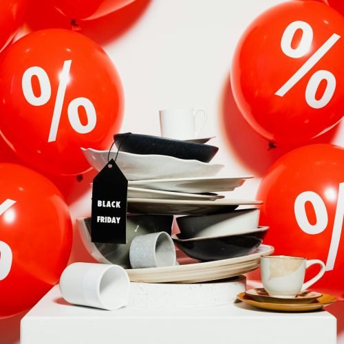 Red balloons with percentage signs surround dishes, highlighting Black Friday sales.