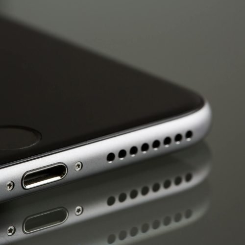 A sleek smartphone close-up highlighting its lightning connector and speaker, reflecting on a surface.