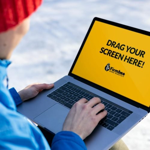 Individual in red hat using a laptop with mockup screen outdoors on a snowy day.
