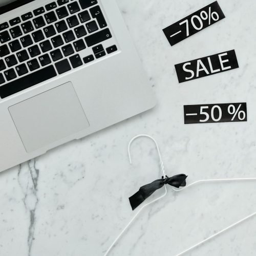 Flat lay of a laptop, hanger, and sale stickers on a marble desk, ideal for Black Friday themes.