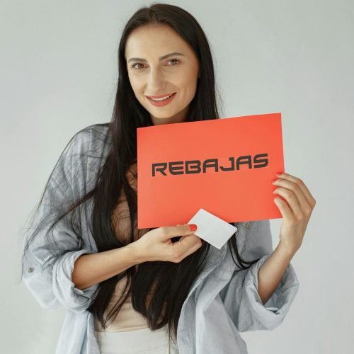 Smiling woman holds a red 'REBajas' sign, promoting sales and discounts.