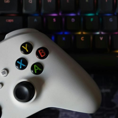 Game controller beside illuminated RGB keyboard, highlighting technology and gaming equipment.
